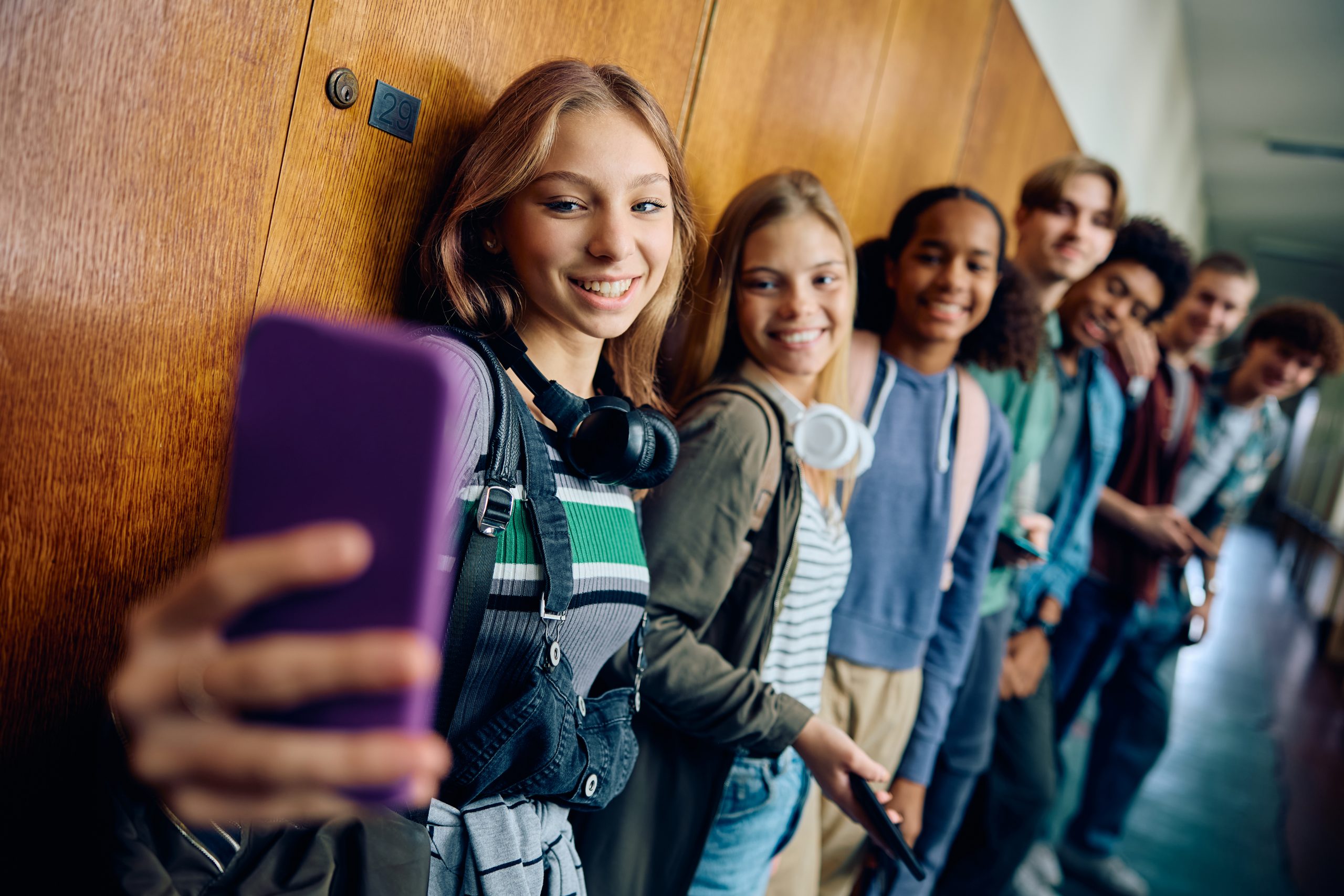 Happy high school student taking selfie with her classmates in a hallway.