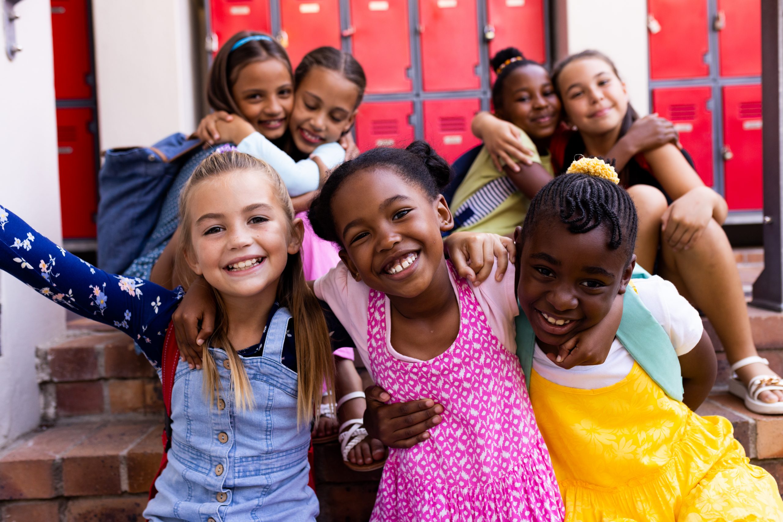 Portrait of diverse happy schoolgirls embracing in elementary school cloakroom. School, learning, childhood, friendship and education, unaltered.